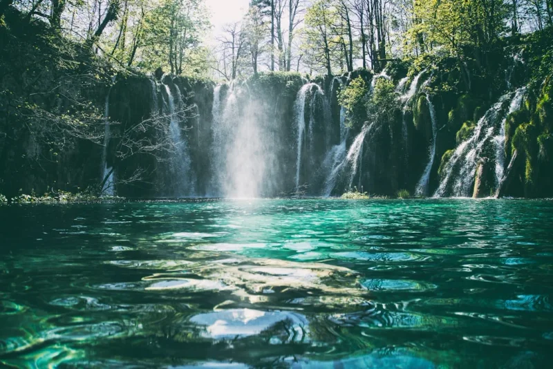 A beautiful multi-tiered waterfall cascading into a turquoise lake surrounded by lush green forest.